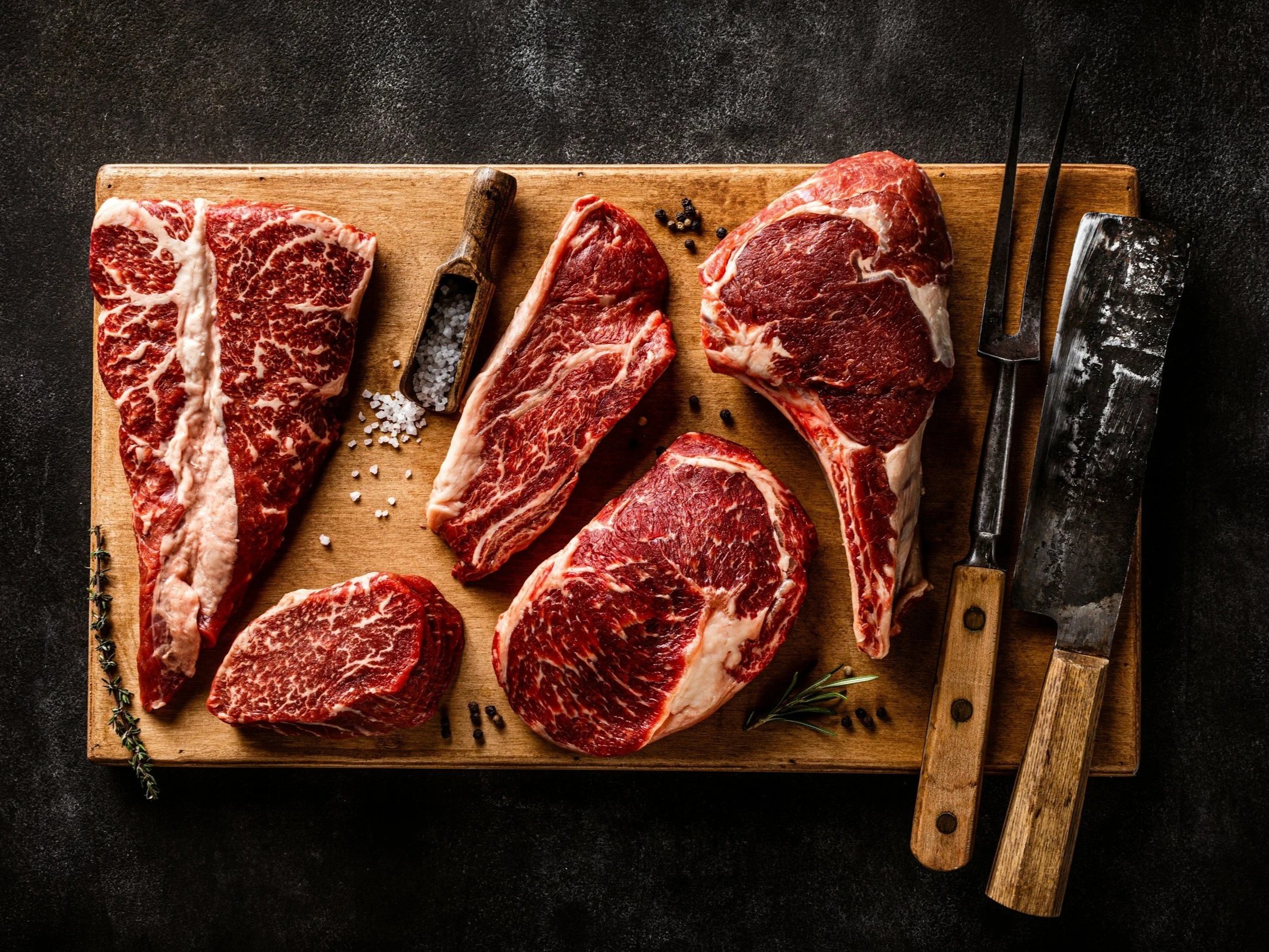unsplash-image-cEJGctX_DgI (7) Assorted cuts of marbled beef displayed on a wooden cutting board, including ribeye, sirloin, and flank steak, accompanied by seasoning and kitchen tools. Ideal for culinary enthusiasts and meat lovers.